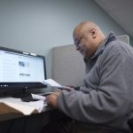 man sitting at computer with papers