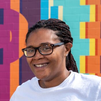 woman with glasses smiling outside in front of colorful wall